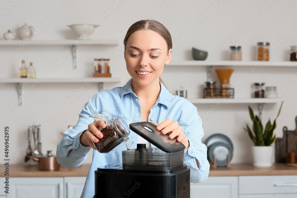 Young woman putting beans into coffee machine in kitchen