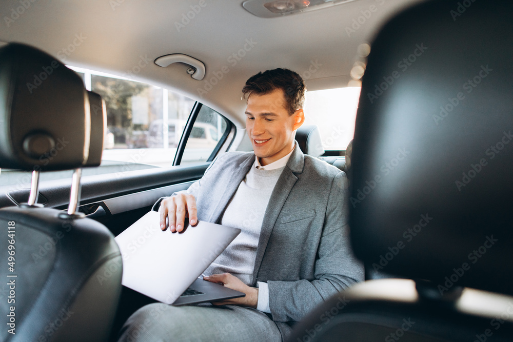 A modern businessman using a laptop computer while sitting in the back seat of a car. A modern businessman using a laptop computer while sitting in the back seat of a car.