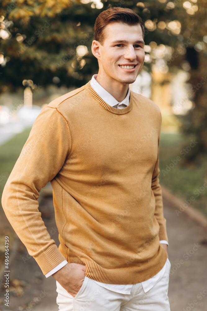 Obraz premium Modern handsome smiling man in yellow and white clothes posing in the park at sunset