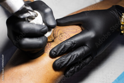 Hands of tattoo artist in black gloves busy with work at tattoo shop. 