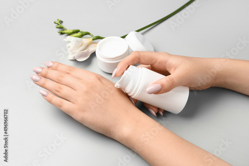 Woman with beautiful manicure applying cream on grey background