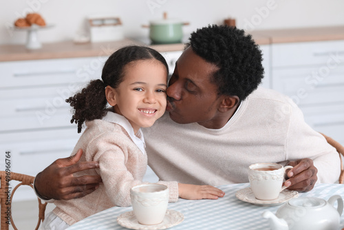Happy African-American man kissing his little daughter in kitchen