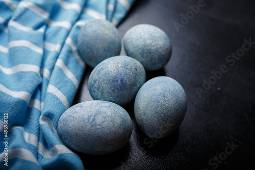 Easter eggs painted blue in white bowl on black wooden background with striped fabric. Close up shot  copy space