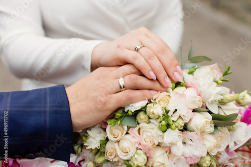 A newly weding couple place their hands on a wedding bouquet showing off their wedding rings.