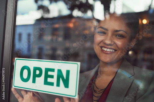 Shes eager to welcome all her customers. Portrait of a young business owner hanging up an open sign on the window of her cafe.