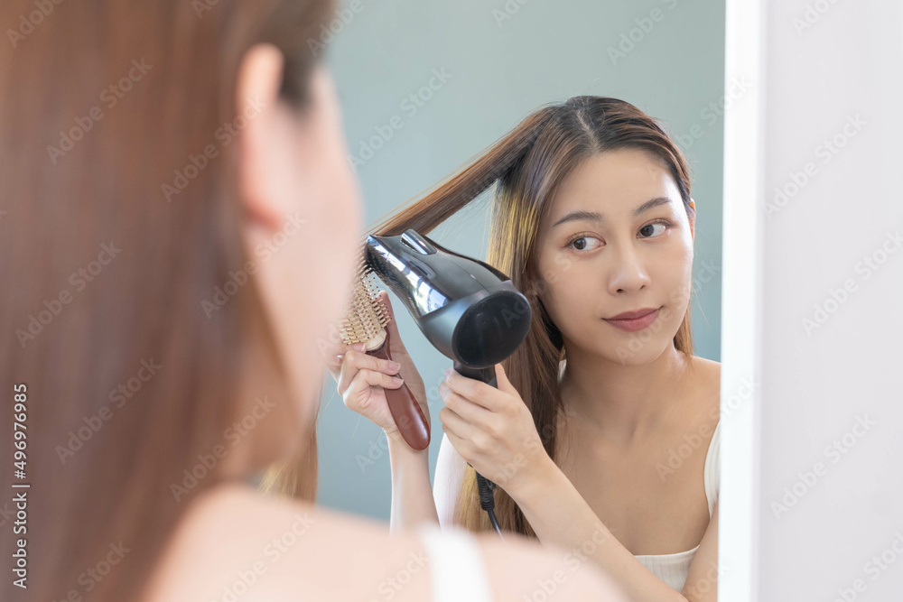 Hair Dryer, happy, asian young woman, girl looking into mirror reflect using hairdryer to dry, blowing long blonde straight after shower at home. Hairdressing, hair treatment and beauty health care. Hair Dryer, happy, asian young woman, girl looking into mirror reflect using hairdryer to dry, blowing long blonde straight after shower at home. Hairdressing, hair treatment and beauty health care.