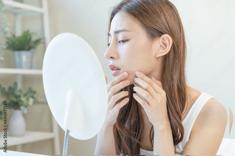 Dermatology, puberty asian young woman, girl looking into mirror, allergy when wear mask and cosmetic, show squeezing pimple spot for removing from face.Beauty care from skin problem by acne treatment Dermatology, puberty asian young woman, girl looking into mirror, allergy when wear mask and cosmetic, show squeezing pimple spot for removing from face.Beauty care from skin problem by acne treatment