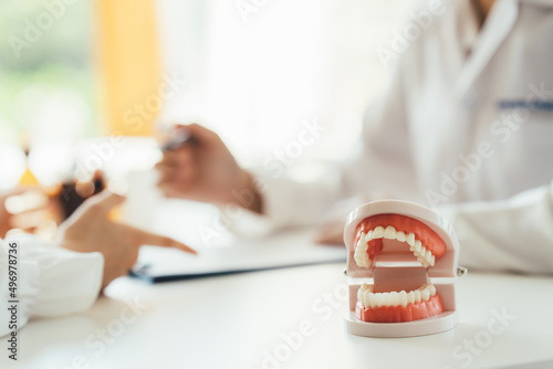 Close up dentist holding teeth model denture and explorer mirror tool for showing and explaining to patient at clinic office , dental healthcare concept.