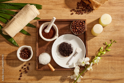 A closeup view of coffee bean and powder salt decorated with wooden tray candles and flower in wooden background for exfoliating advertising , mixture of coffee and salt 