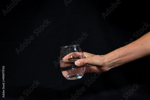 hand offering glass with pure water, black background