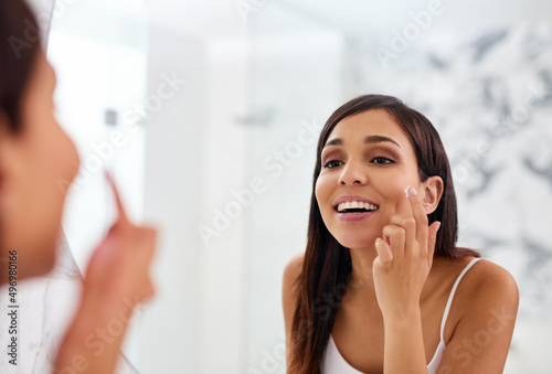 Her daily routine keeps her glowing for days. Shot of an attractive young woman applying moisturizer to her face in the bathroom.