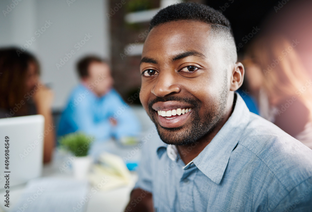 Im here to break new grounds. Portrait of a young designer sitting in an office with his colleagues in the background. Im here to break new grounds. Portrait of a young designer sitting in an office with his colleagues in the background.