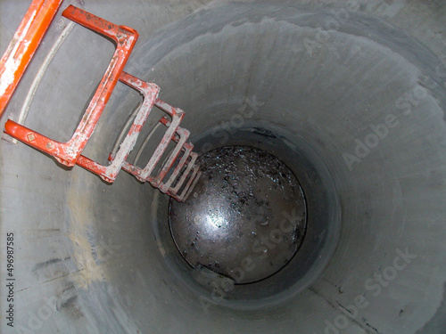 Canvas Print Looking into an open concrete manhole with step rungs leading down stagnant wate