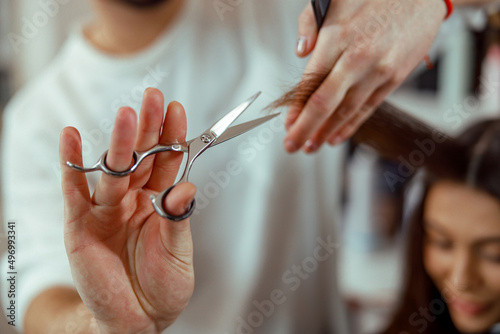 Close up of hairdresser hands holding hair strand while cutting hair of female client. Hairstyling