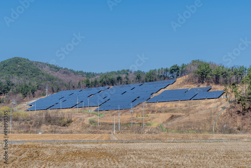 Solar panels on side of hill in countryside under clear blue sky.