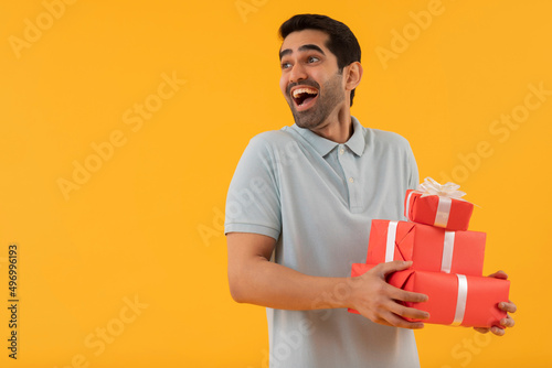 Excited young man holding gifts in his hands against yellow background