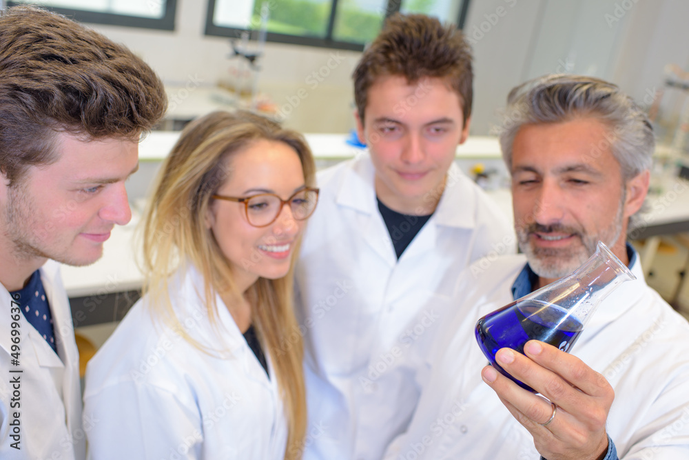Science teacher and students looking at liquid in glass flask Science teacher and students looking at liquid in glass flask