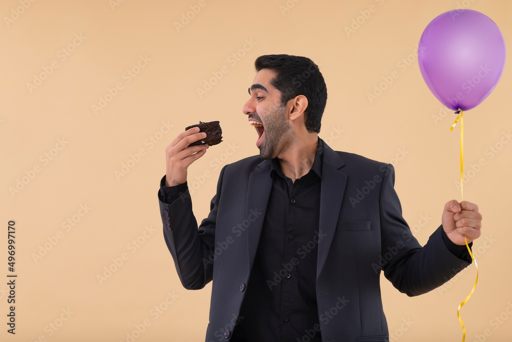 Naklejka premium Portrait of happy businessman holding balloon in one hand and eating cake with other