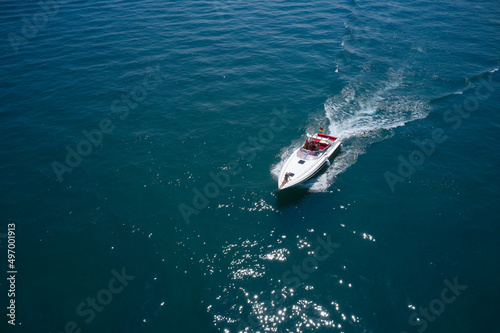 Drone view of a moving white boat on the water. Speedboat moves fast on the water top view. Speed boat with red seats aerial view. People rest on a boat. © Berg