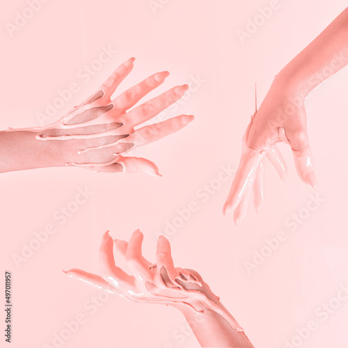 Creative concept of a raised hands dipped in peachy paint in the air. Pastel pink background.