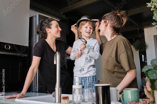 Happy little boy playing in kitchen together with his homosexual mothers
