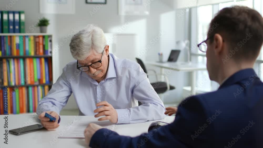 Aged man read agreement and pay insurance fee with credit card in modern company