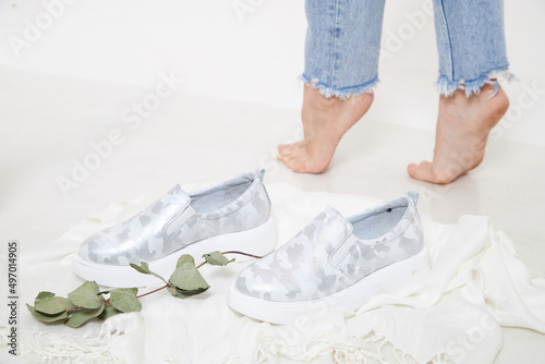 White and silver beautiful fashionable female loafers shoes on leg of girl or woman. Studio shoot on white background for a magazine, website in Internet or catalog