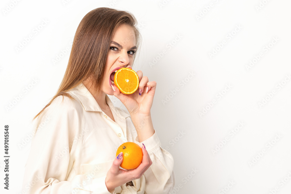 Young caucasian pretty cunning brunette woman biting one orange half and looking at the camera wearing a white shirt over white background Young caucasian pretty cunning brunette woman biting one orange half and looking at the camera wearing a white shirt over white background