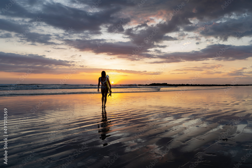 Surfer girl on the beach at sunset. Surf silhouette of woman walking with surfboard at golden hour beautiful colors