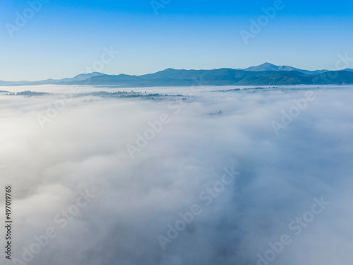 Flight over fog in Ukrainian Carpathians in summer. Mountains on the horizon. A thick layer of fog covers the mountains with a continuous carpet. Aerial drone view.