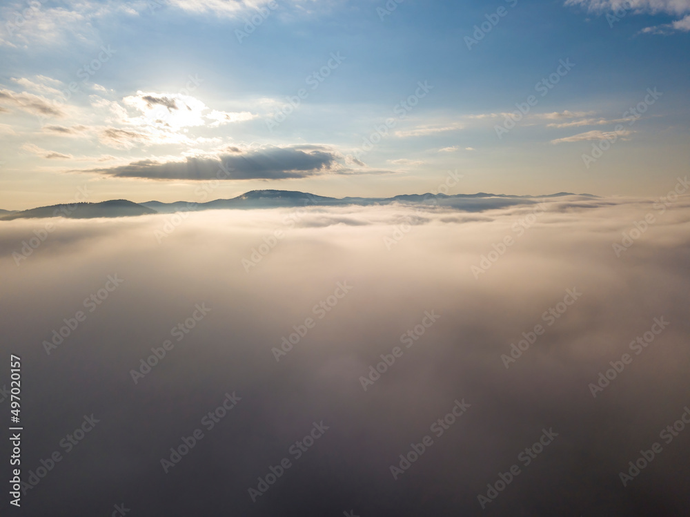 Flight over fog in Ukrainian Carpathians in summer. Mountains on the horizon. A thick layer of fog covers the mountains with a continuous carpet. Aerial drone view.