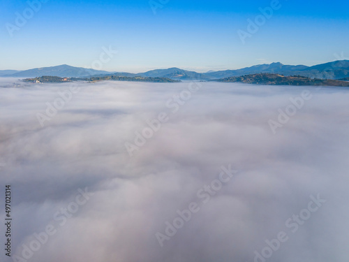 Flight over fog in Ukrainian Carpathians in summer. Mountains on the horizon. A thick layer of fog covers the mountains with a continuous carpet. Aerial drone view.