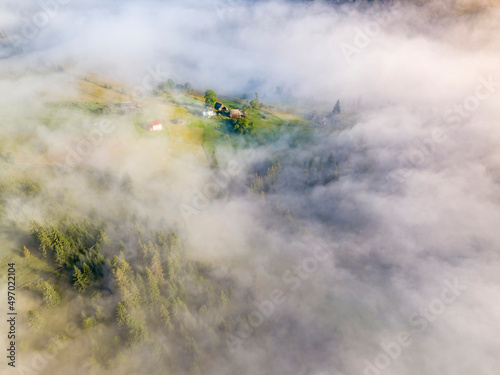 Fog envelops the mountain forest. The rays of the rising sun break through the fog. Aerial drone view.