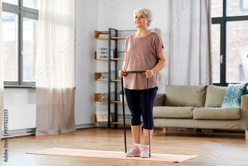 sport, fitness and healthy lifestyle concept - smiling senior woman exercising with resistance band on mat at home