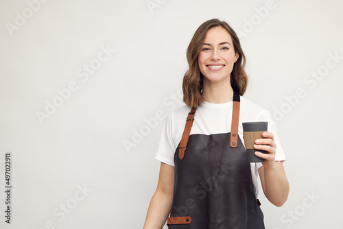 Portrait of beautiful young barista woman looking in camera and smiling, while holding a to-go coffee in hand. Isolated on white background.	