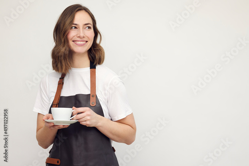 Beautiful young barista woman smiling and serving a cup of coffee. Isolated on white background looking professional.