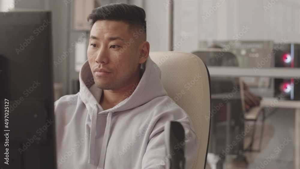 Waist up slowmo of concentrated Asian male programmer sitting in front of pc in office developing computer game Waist up slowmo of concentrated Asian male programmer sitting in front of pc in office developing computer game