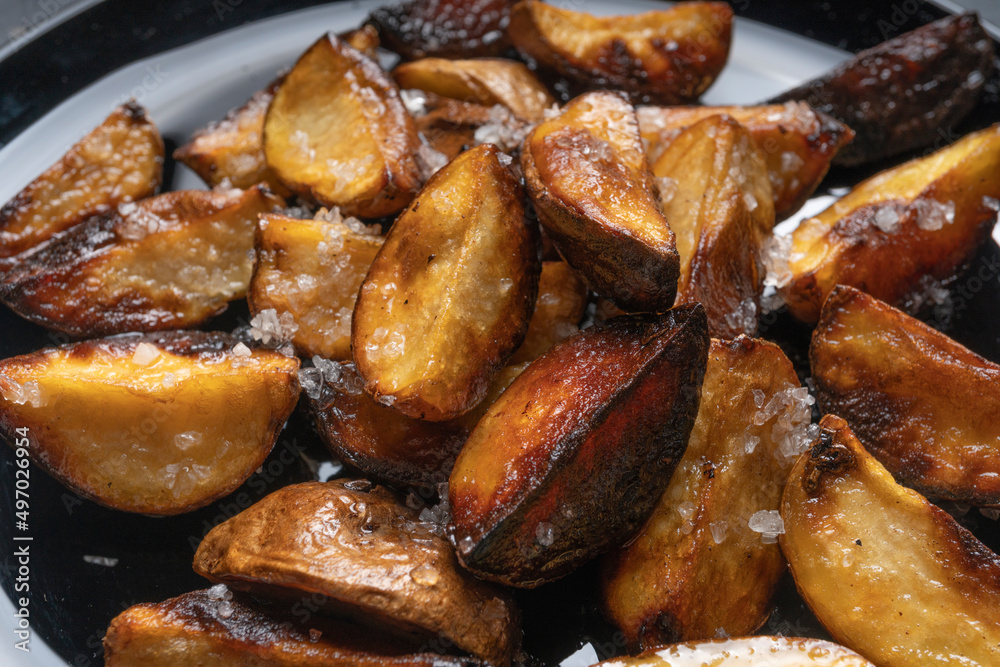 Rustic fried potatoes on a black dish on the table, top view