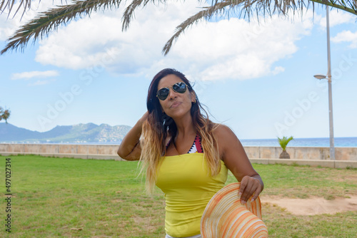 portrait of a latin woman smiling, having fun, on vacation in mallorca posing on a warm spring summer day, under a palm tree, hollidays concept photo