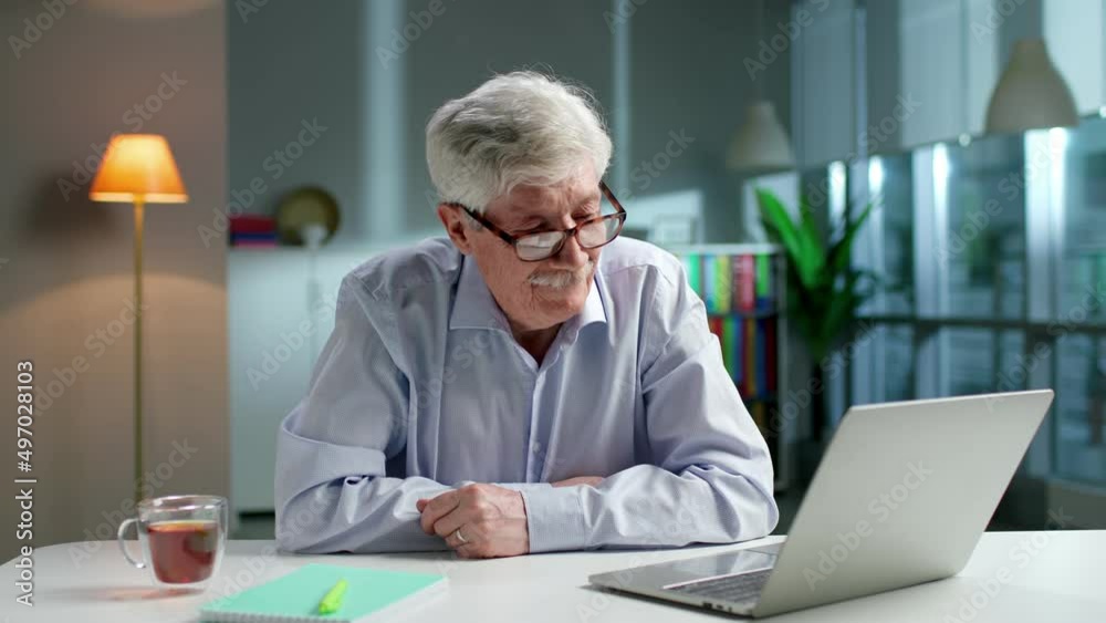 Elderly man having video call on laptop sitting at desk in living room Elderly man having video call on laptop sitting at desk in living room
