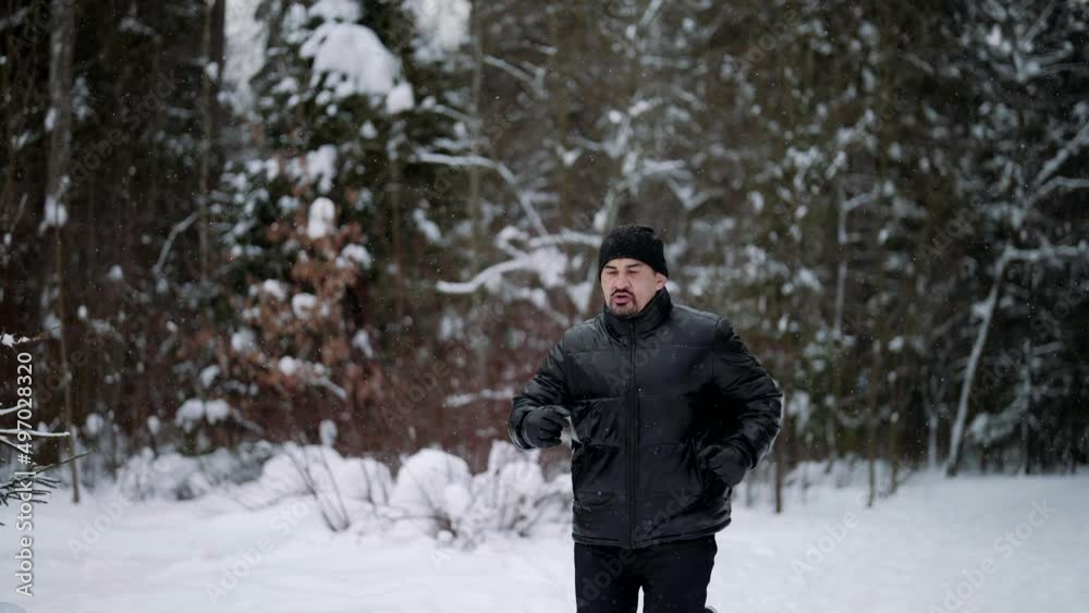 middle-aged man is training in forest in winter day, running over snow and breathing cold air middle-aged man is training in forest in winter day, running over snow and breathing cold air