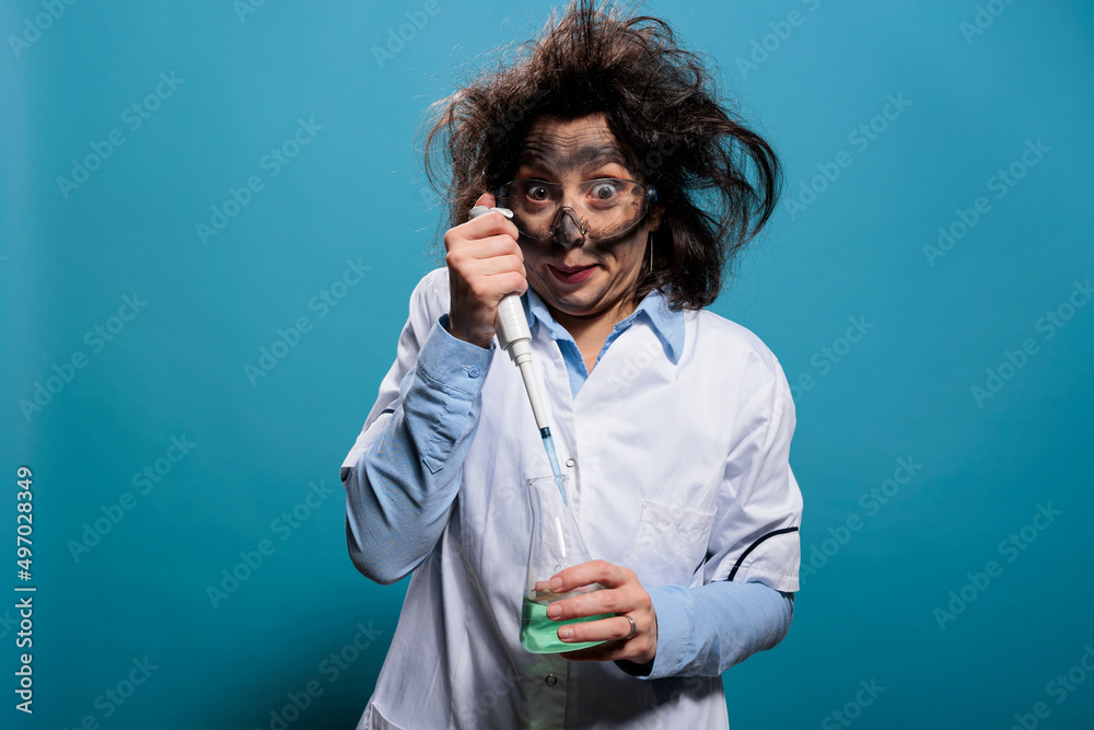 Crazy mad scientist using pipette to drip chemical compound inside glass beaker filled with liquid toxic substance. Wacky chemist with pipette and chemistry flask on blue background. Studio shot. Crazy mad scientist using pipette to drip chemical compound inside glass beaker filled with liquid toxic substance. Wacky chemist with pipette and chemistry flask on blue background. Studio shot.