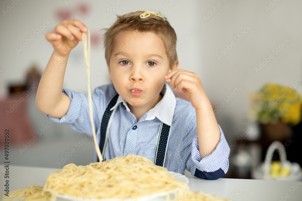 Cute preschool child, blond boy, eating spaghetti at home, making a mess everywhere Cute preschool child, blond boy, eating spaghetti at home, making a mess everywhere