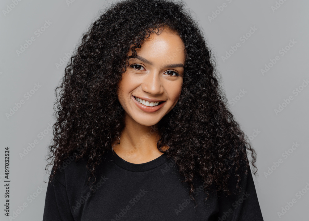 Woman with gentle smile, looks positively at camera, wears casual black clothes, isolated on grey background Woman with gentle smile, looks positively at camera, wears casual black clothes, isolated on grey background