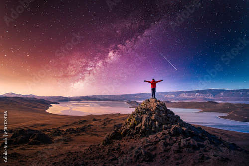 Traveler man wear red clothes and raising arm standing on mountain at with milky way in Lake Baikal, Siberia, Russia.