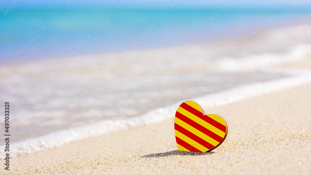 Obraz premium Flag of the Catalonia in the shape of a heart on a sandy beach. The concept of the best vacation in Catalonia resorts