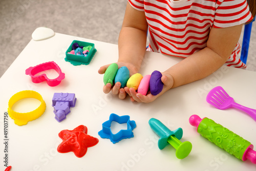 closeup children's hands with multicolored plasticine or playdough on white table with toys, children's creativity concept photo