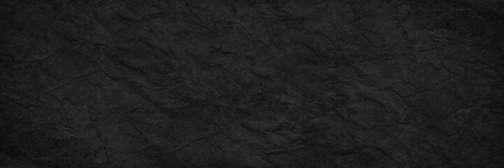 Abstract black background. Wide banner. Dark rock surface texture. Close-up. Stone rough background with copy space for design. Panoramic.