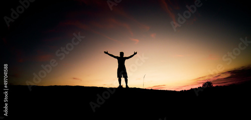 The silhouette of a man is standing with his hands up in happiness.