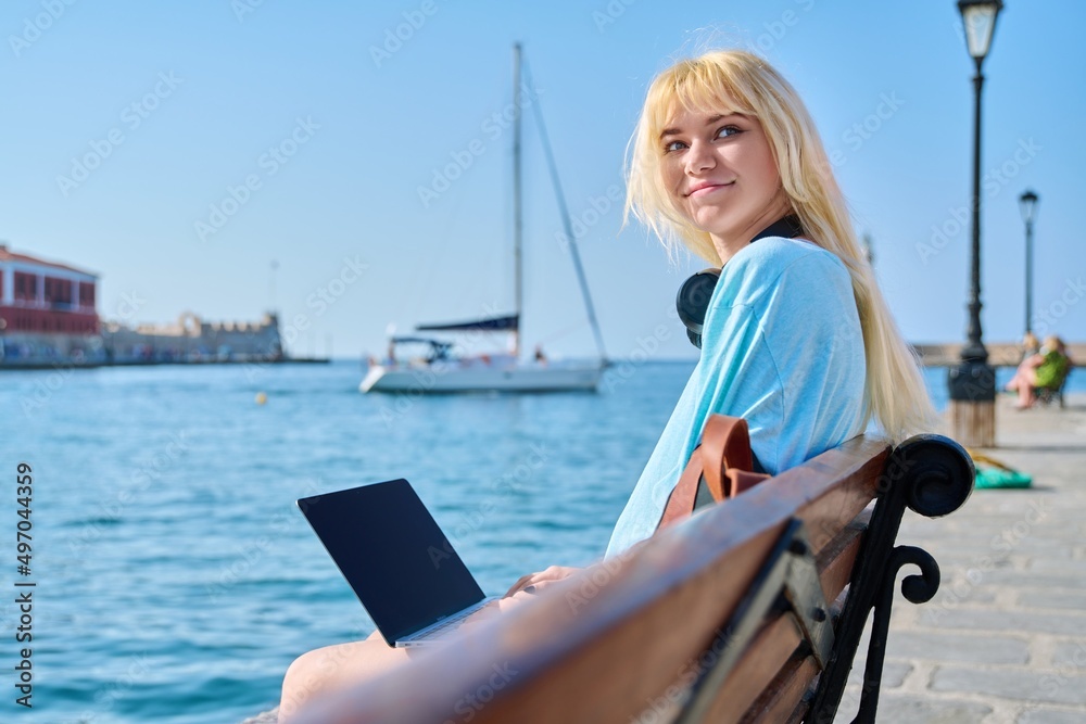 Fototapeta premium Young woman relaxing in headphones with a laptop on the seashore